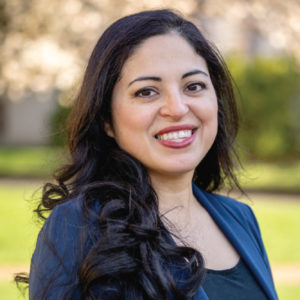 A smiling photo of Andrea Salazar Phd , Counseling Center. Andrea has long black hair and is wearing a black top with a blue jacket.