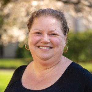 A smiling photo of Anne Swenson Phd , Counseling Center. Anne has tied blonde hair and is wearing a black t shirt.