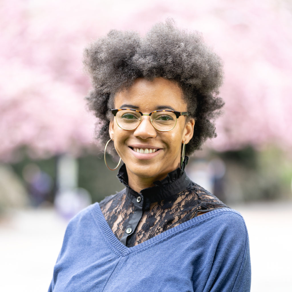 A smiling photo of Paige Sechrest Epic Training Specialist. Paige has black curly hair and is wearing a blue/black top and glasses.