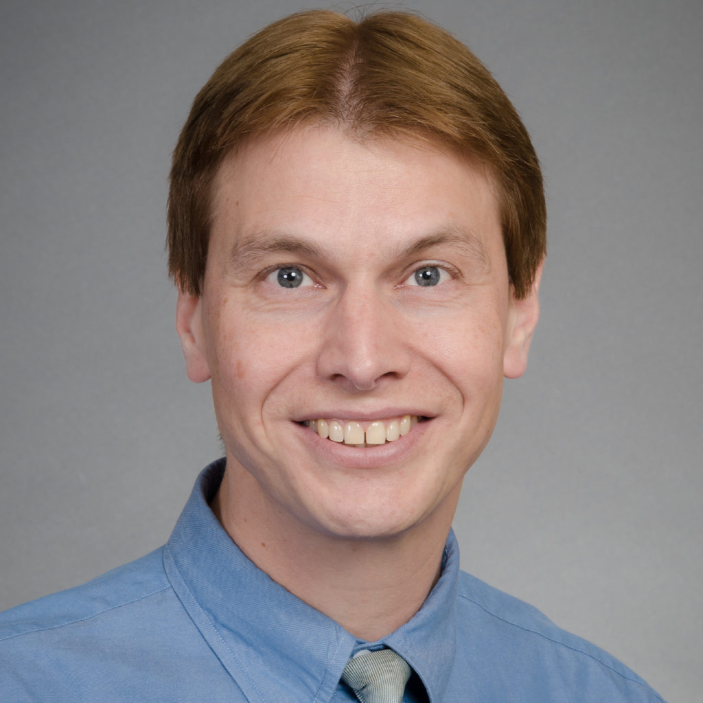 A smiling photo of Doug Kleemann. Doug has short brown hair and is wearing a blue shirt.