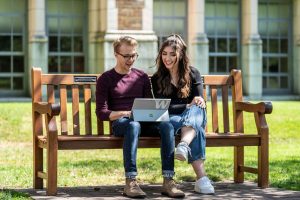 Two friends sitting on a bench and looking at the laptop