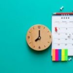 A clock and calendar rest on a turquoise-colored wall.