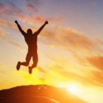 The silhouette of a joyful person jumping on a hill with the sun behind them.