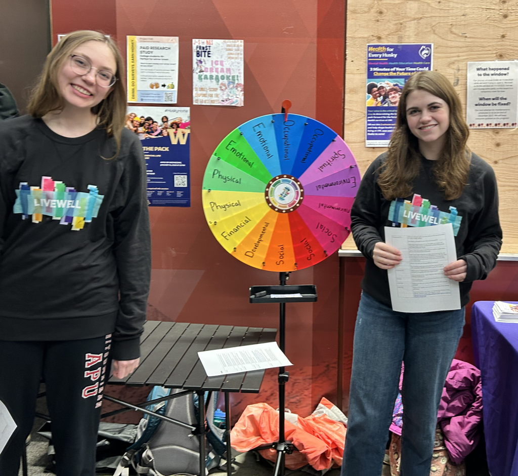 Peer Health Educators at a tabling event next to LiveWell well-being wheel